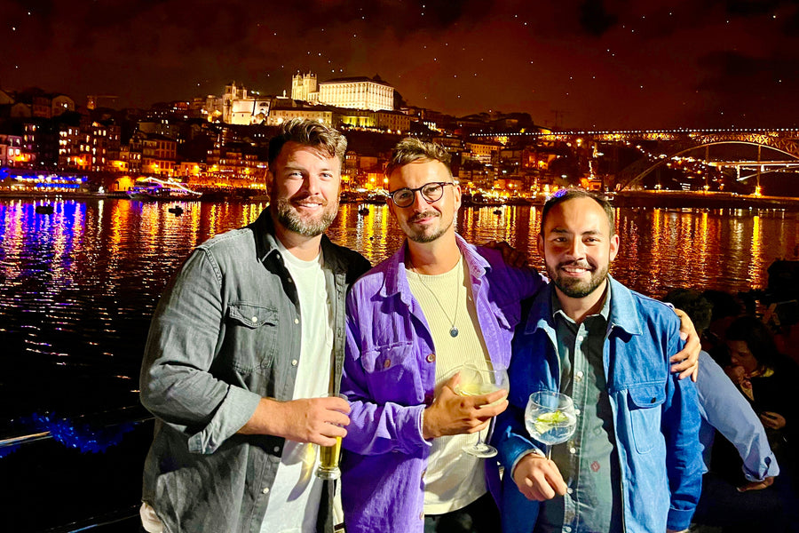 Three men standing together at night by a waterfront with a cityscape in the background.